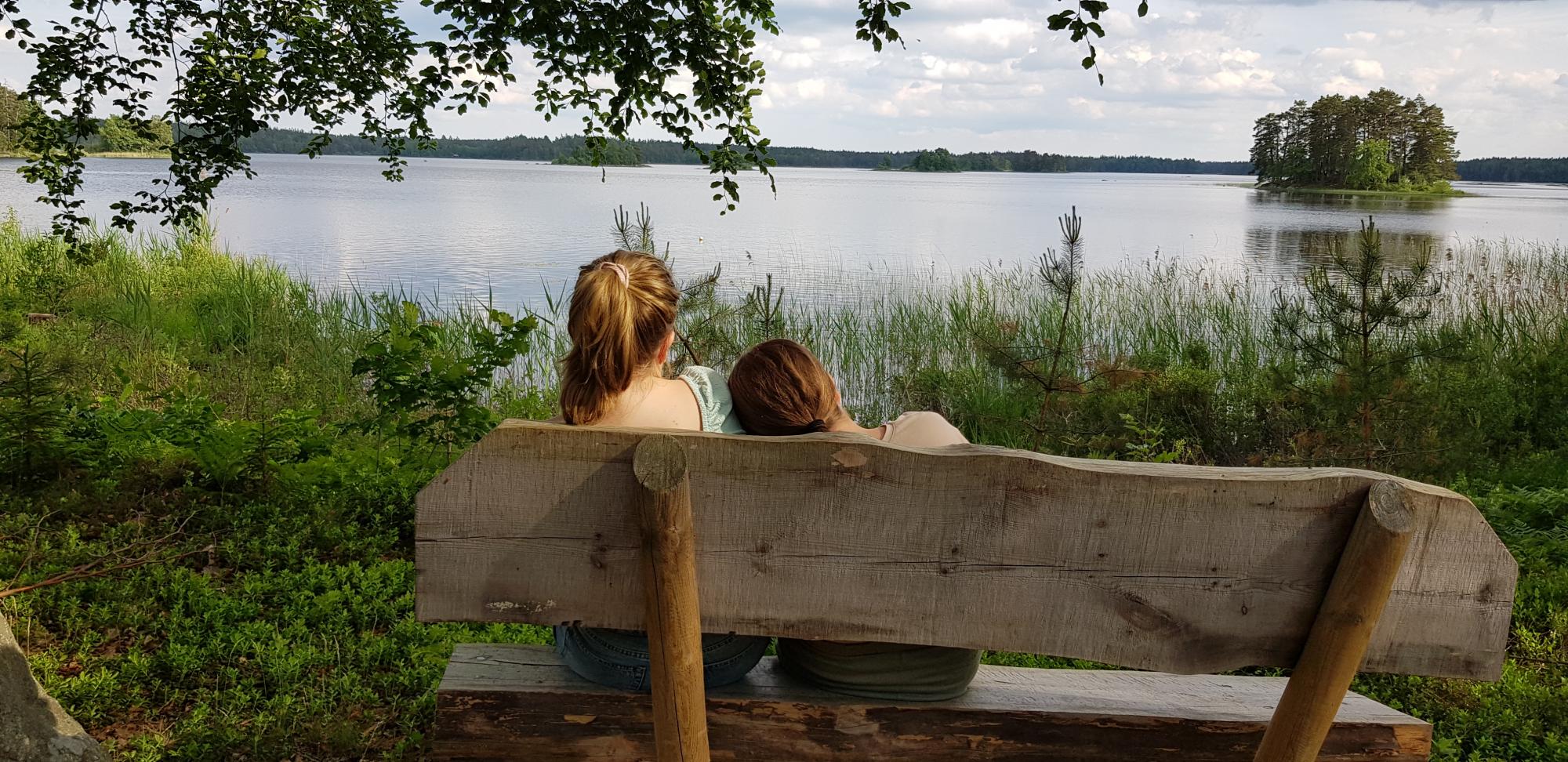 Två barn sitter på en bänk och tittar ut över sjö